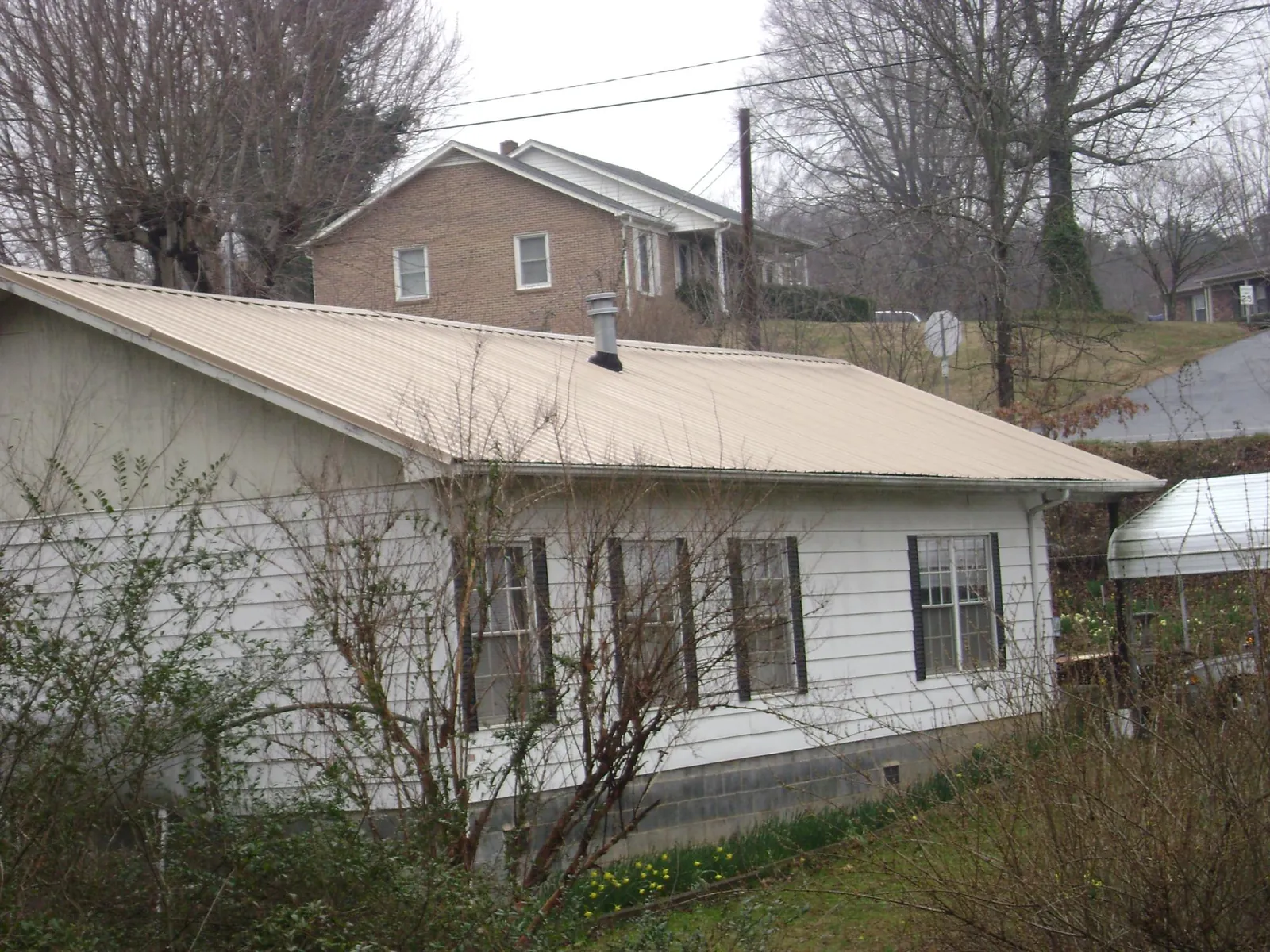 Tan metal roof on a white sided house set into a hillside — Commercial Roofing by Roofing Brothers in Sunset